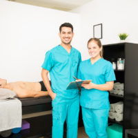 Physiotherapy Professionals With Clipboard Standing By Patient In Bed Young physiotherapy professionals with clipboard standing by patient in bed at hospital